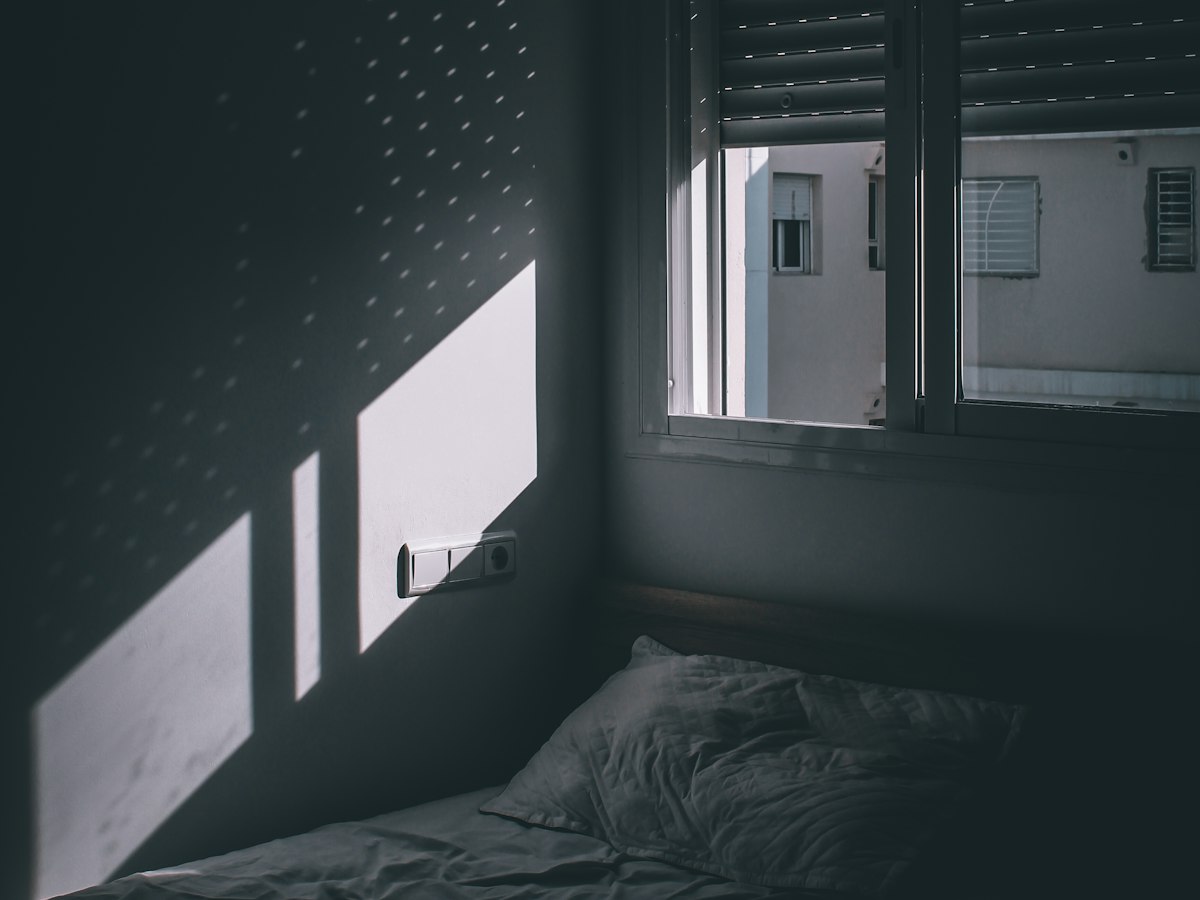 Abgedunkeltes Schlafzimmer, Licht fällt nur durch die Schlitze des Rollladens