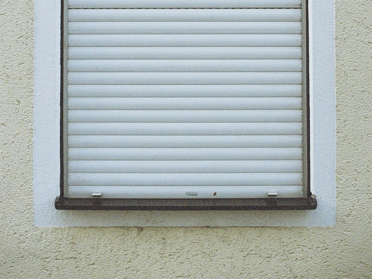 Geschlossener weißer Rollladen an einer hellen Hauswand